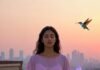 Why Yoga Can Be Your Shortcut to Inner Peace (Backed by Science) a frazzled-looking person in loose sweatpants doing a very imperfect lotus pose on a concrete rooftop at golden hour
